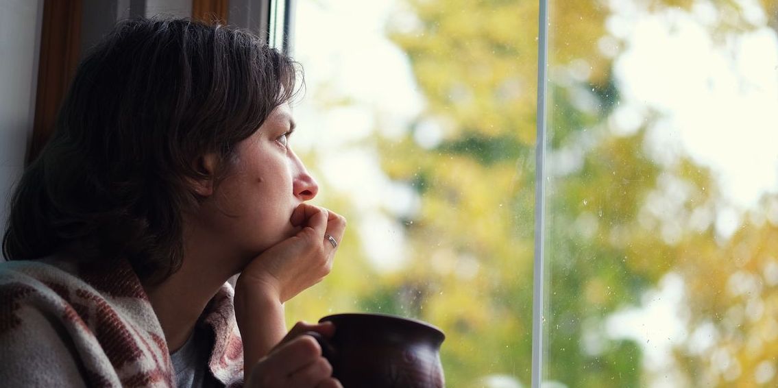 depressed woman looking out window at seasonal changes